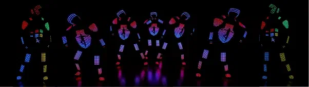 Seven Tron Pixel dancers in a row on a black stage, their LED pixel suits glowing red, blue, pink and green