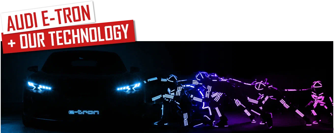 Audi E-Tron + our technology – red and white banners above a dark Audi e-tron with glowing blue headlights and a lit e-tron logo, next to Tron dancers in glowing blue and purple LED suits pushing towards it, under a glowing “Volvo Art Session” sign