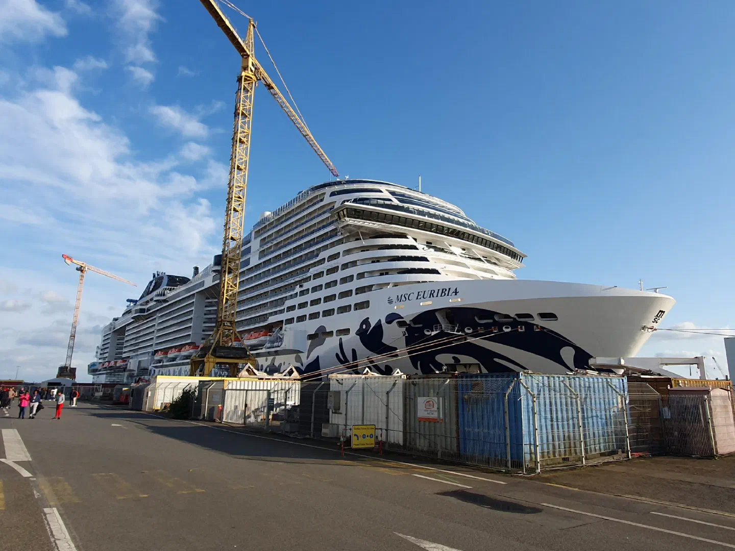 The MSC Euribia cruise ship at a quay in France with a yellow crane beside it and construction fences in front