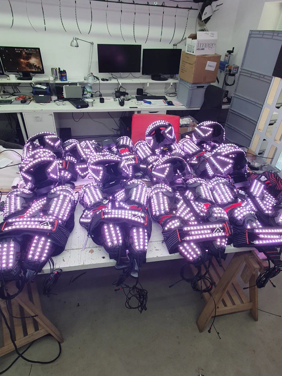 Freshly made LED suits – helmets, chest pieces and arm and leg parts glowing purple – laid out on the tables of our workshop