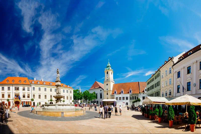 Bratislava’s Main Square on a sunny day – the Roland Fountain, the Old Town Hall tower and café sunshades in front of historic buildings