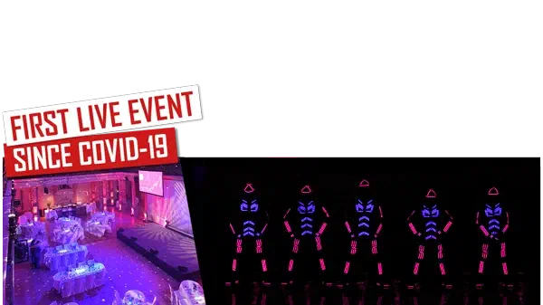 First live event since Covid-19 – red and white labels above a festive hall with round tables lit in purple, next to five dancers in LED suits glowing blue and pink on a dark stage