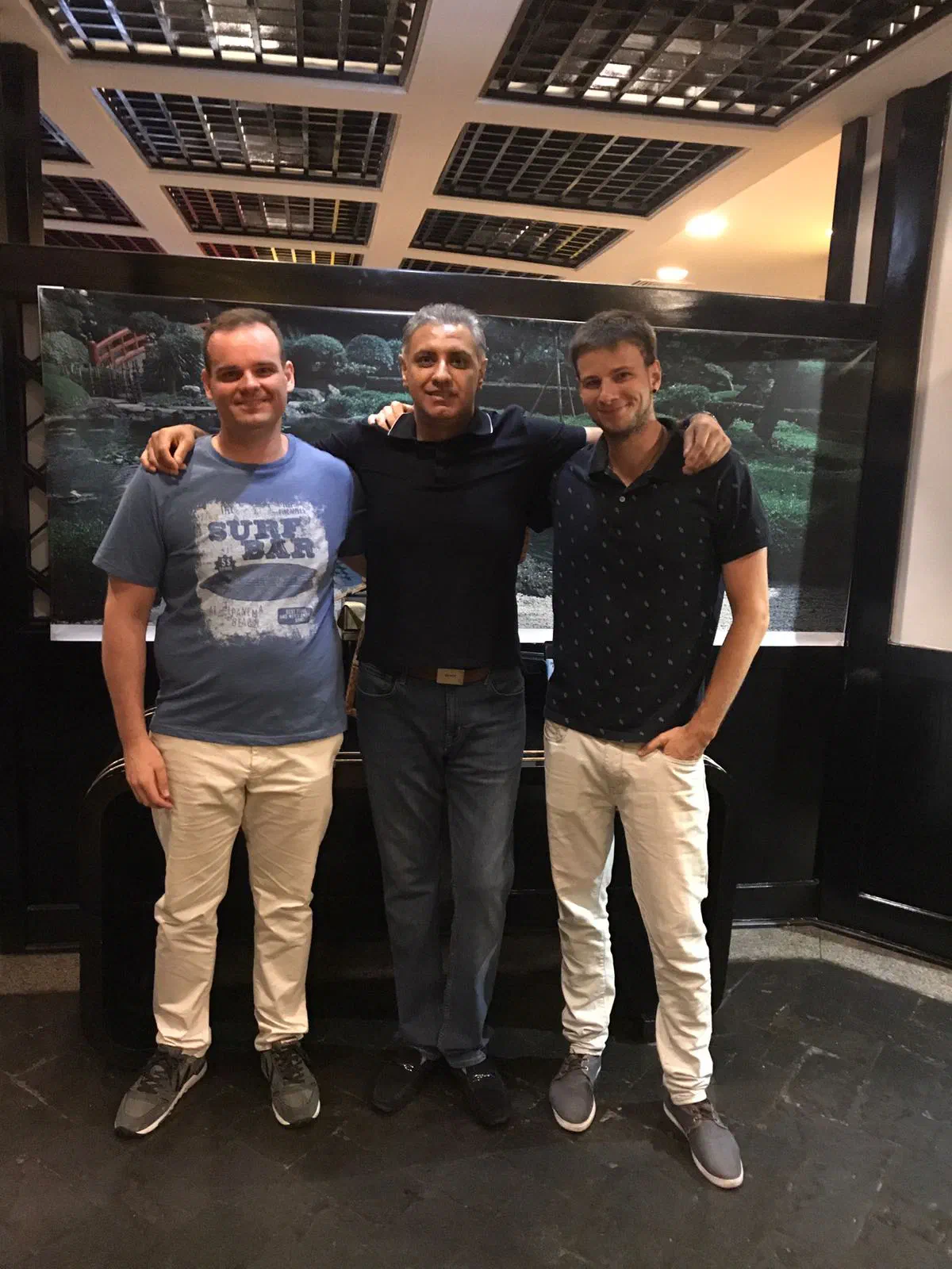 Michal, Ahmer (our client) and Richie standing arm in arm indoors, in front of a large photo of a Japanese garden