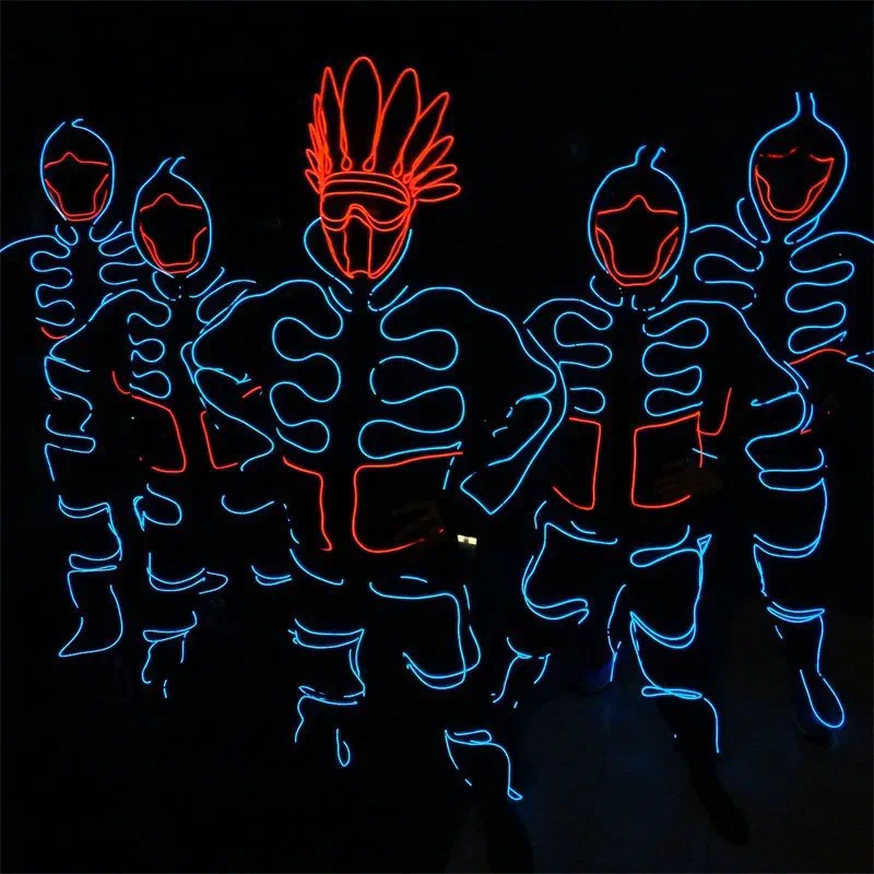 Five dancers in EL wire suits glowing blue and red in the dark, the one in the middle with a red feather headdress