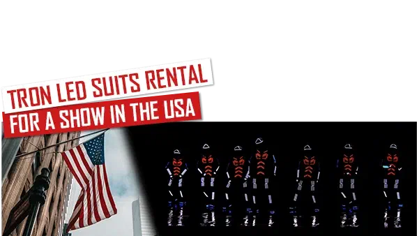 Prenájom LED kostýmov Tron pre show v USA – červené a biele bannery nad americkou vlajkou na budove, vedľa sedem tanečníkov v žiariacich LED kostýmoch s červeným vzorom oka a lomených pruhov na hrudi