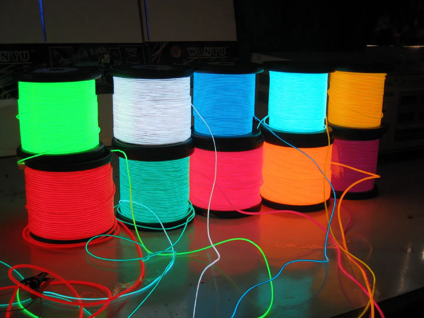 Ten spools of glowing EL wire in different colours – green, white, blue, cyan, yellow, red, turquoise, pink, orange and magenta – with loose wire ends on a table