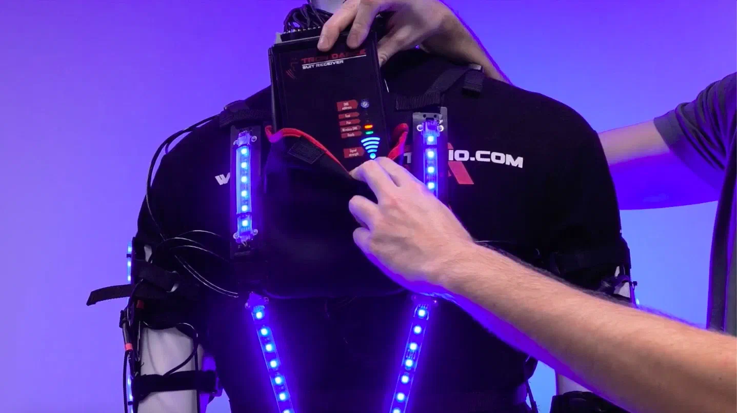 Back of a Tron Dance suit on a mannequin – a hand lifts the Tron Dance suit receiver out of its pouch between LED strips glowing blue
