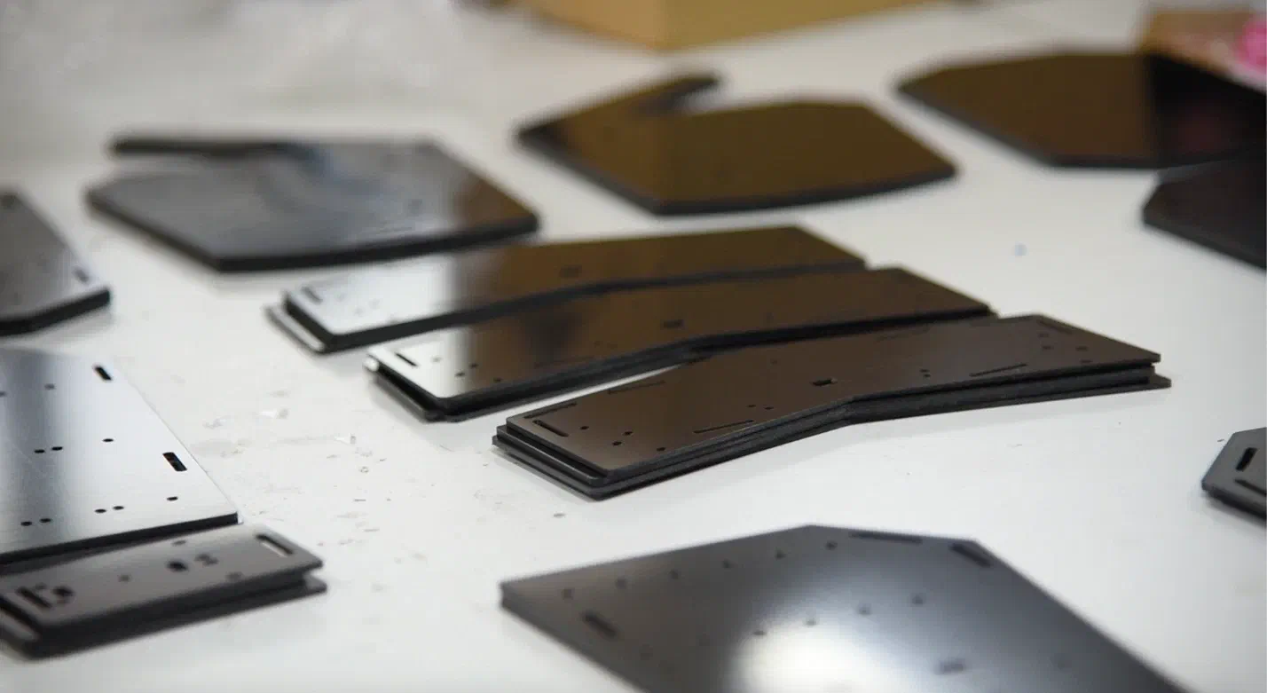 Cut black plastic plates for the body parts of an LED suit lying on a white table