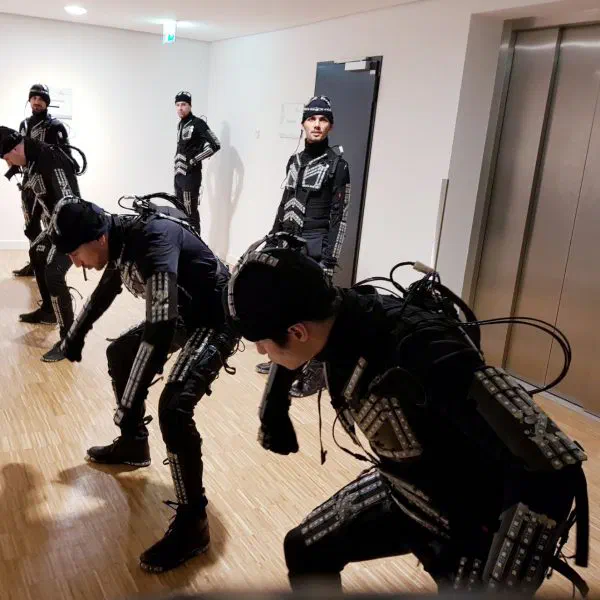 Tron dancers in black LED suits with unlit LED stripes and cables warming up in a hallway in front of a lift before the show