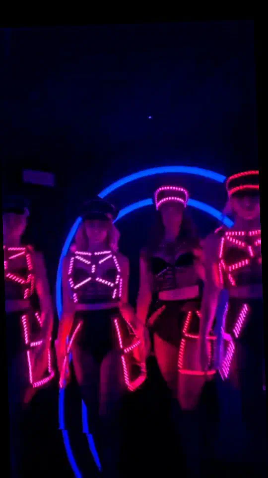 Four dancers in black Dolls costumes and caps lined with glowing pink and red LEDs in front of a blue neon ring – cover picture of the Tron Girls Instagram reel from the Let’s Dance spot