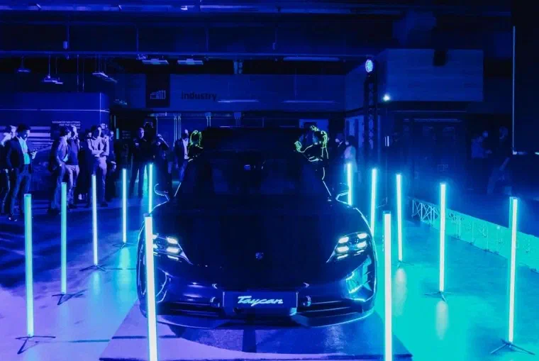 The unveiled Porsche Taycan between glowing turquoise light poles, two Tron Girls in LED suits behind it and guests watching