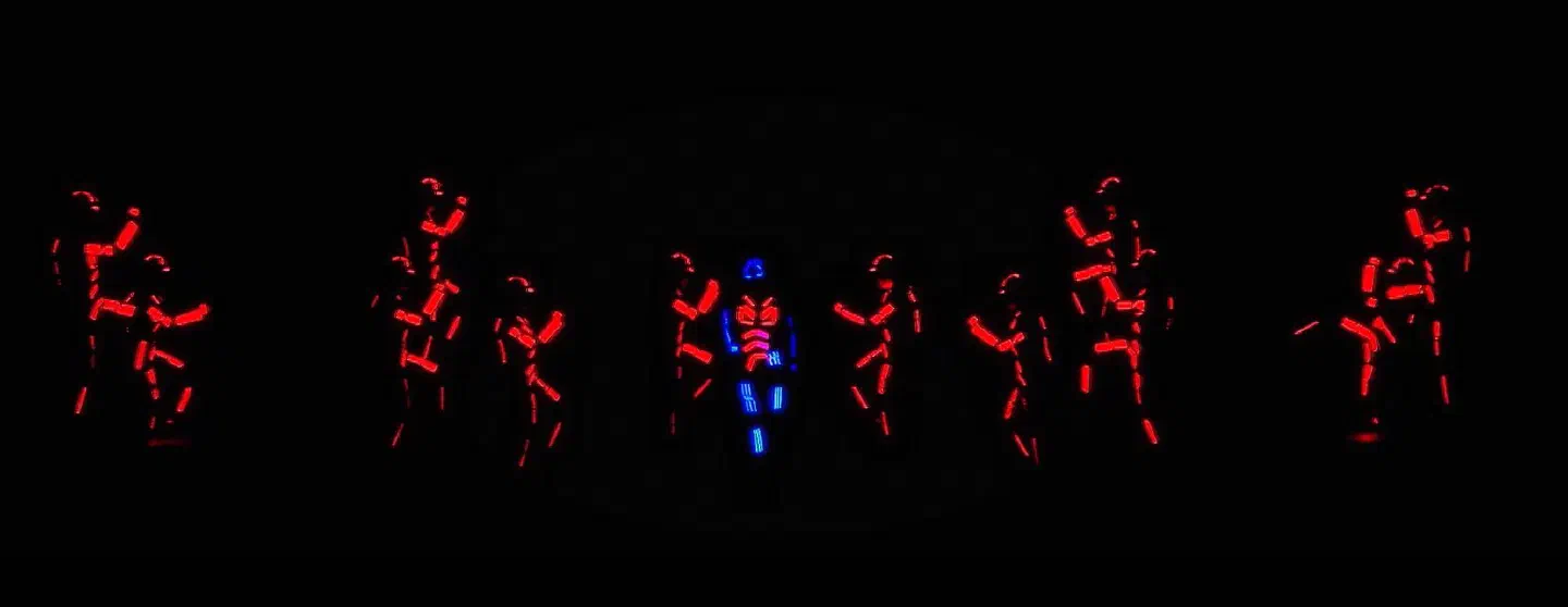 Rad tanečníkov v červených LED kostýmoch okolo jedného tanečníka v modrom LED kostýme na tmavom pódiu – show Dance Dance Dance pre holandskú televíziu