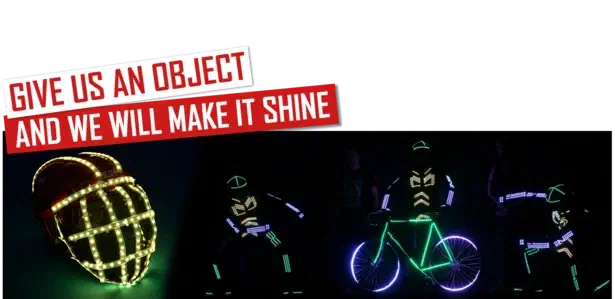 Give us an object and we will make it shine – red and white banners above a helmet wrapped in glowing LED strips and three Tron dancers in LED suits around a bicycle lit with green and purple LEDs