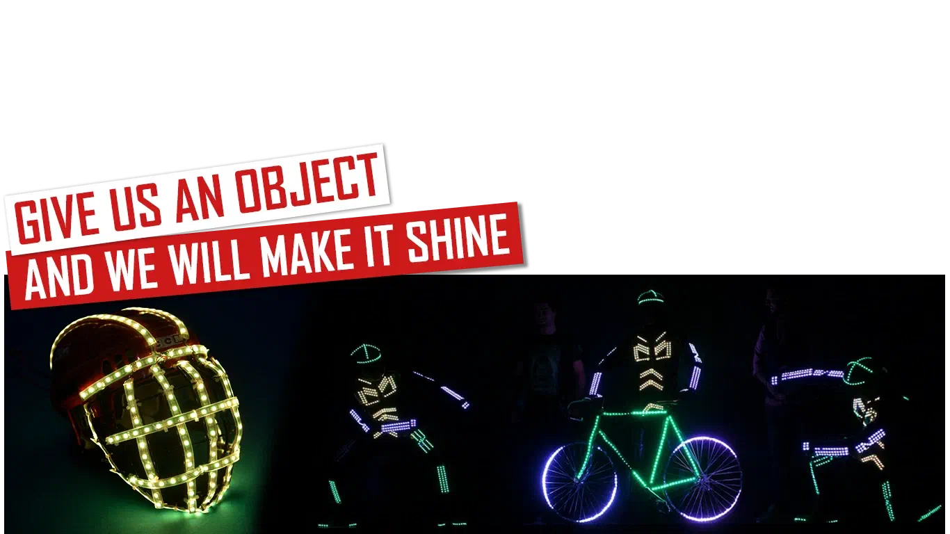 Give us an object and we will make it shine – red and white banners above a helmet wrapped in glowing LED strips and three Tron dancers in LED suits around a bicycle lit with green and purple LEDs