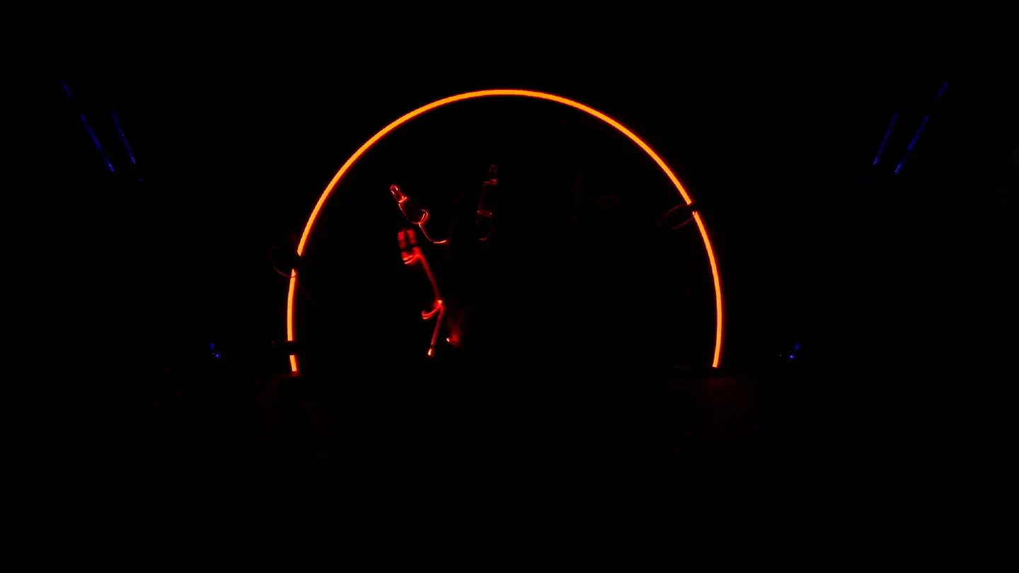 A glowing orange arc on the LED wall frames a Tron Girl in red-lit LED stripes in the dark studio, blue light beams at the sides