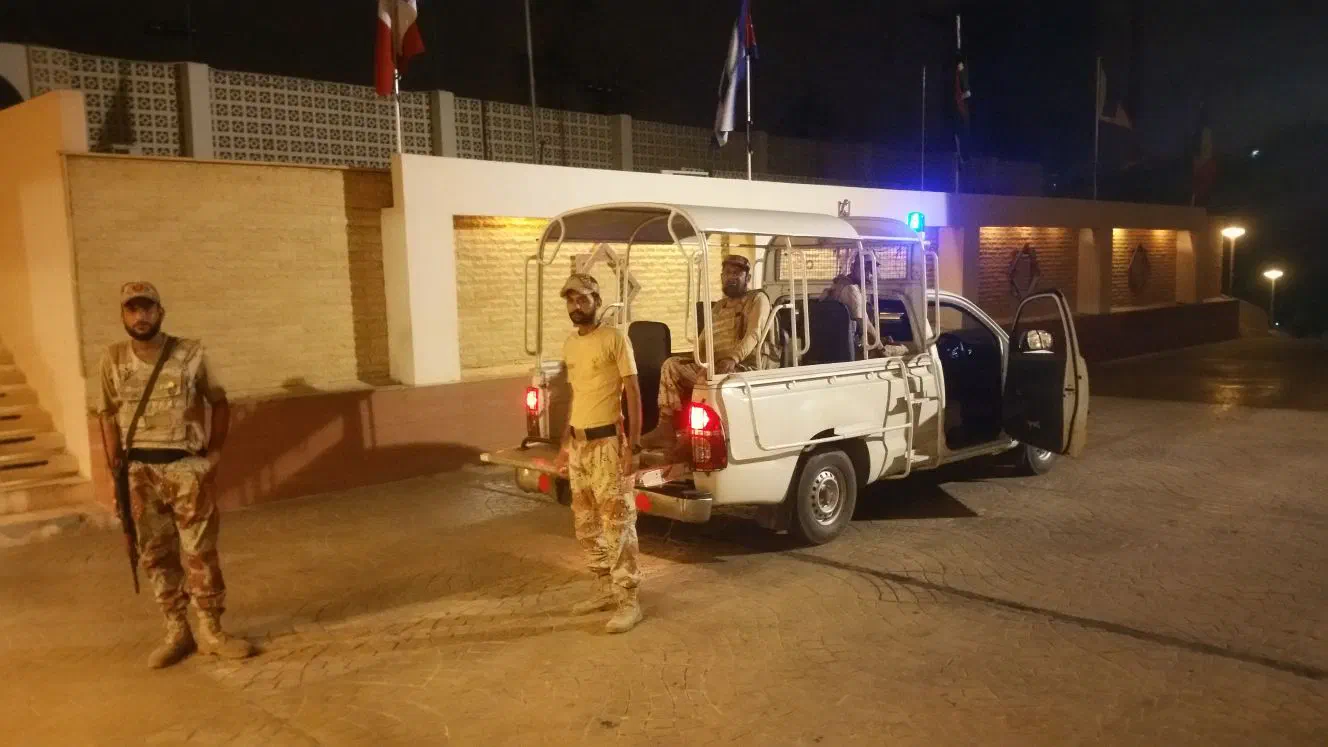 Pakistani soldiers in camouflage uniforms, one of them with a rifle, beside their white pick-up truck in front of the hotel at night