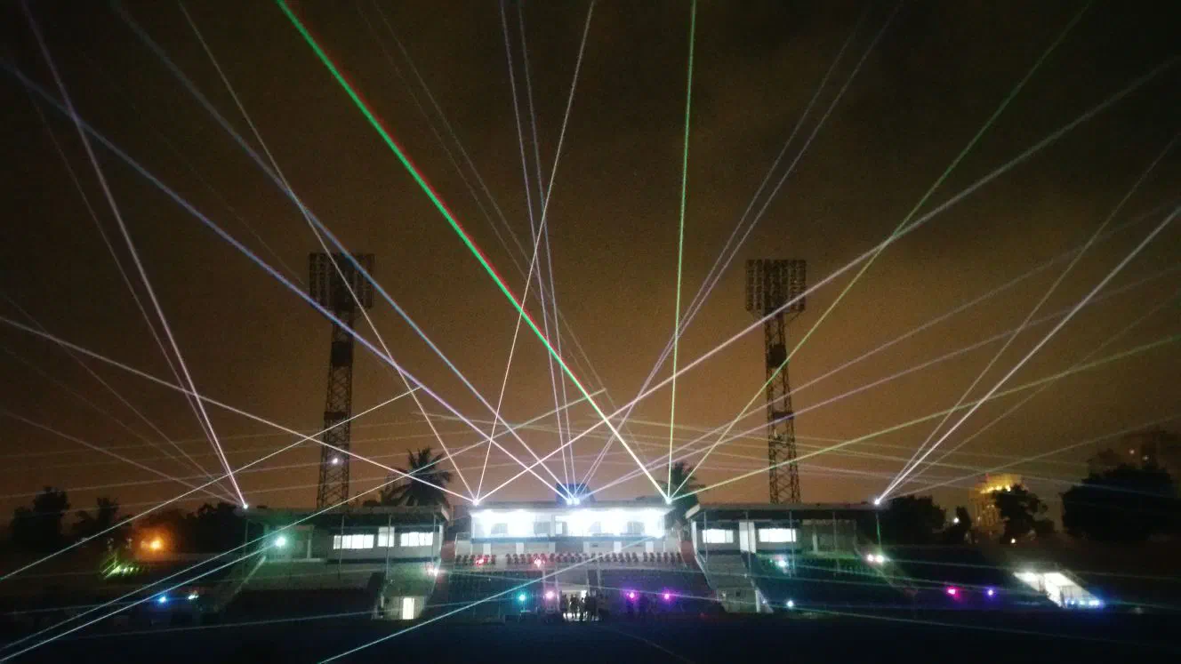 White, green and red laser beams fanning out into the night sky from the stadium stand, between two floodlight towers