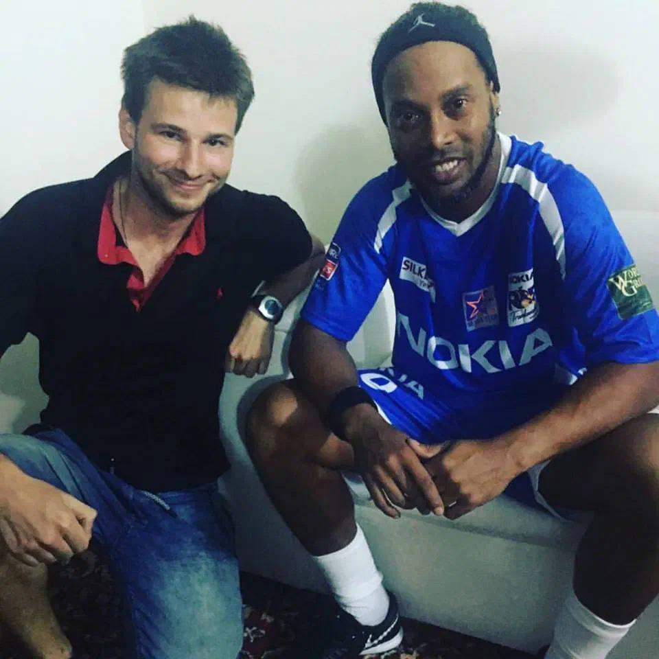 The author with Ronaldinho, who wears a blue Nokia football shirt and a black headband, sitting on a white sofa in his changing room