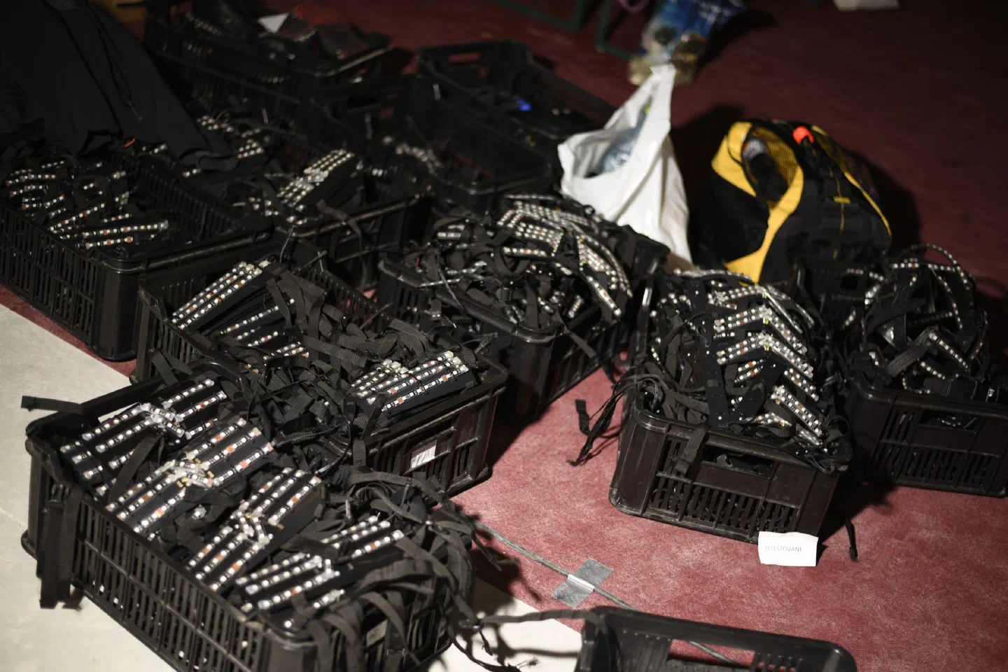 LED suit parts with LED strips and black straps packed in black plastic crates on a red floor, next to a black and yellow backpack
