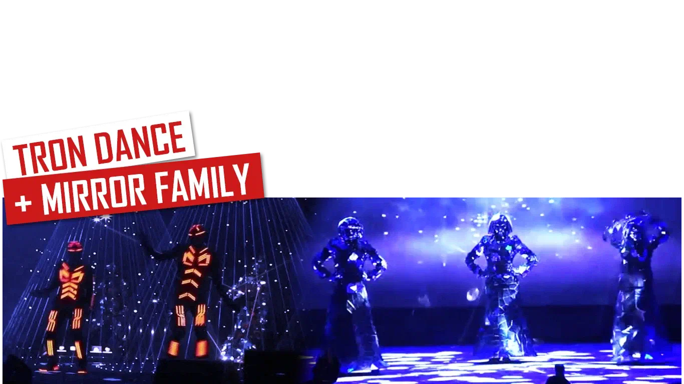 Tron Dance + Mirror Family – red and white labels above two Tron dancers in glowing orange LED suits among blue laser beams and three Mirror Family dancers in mirror costumes on a blue-lit stage