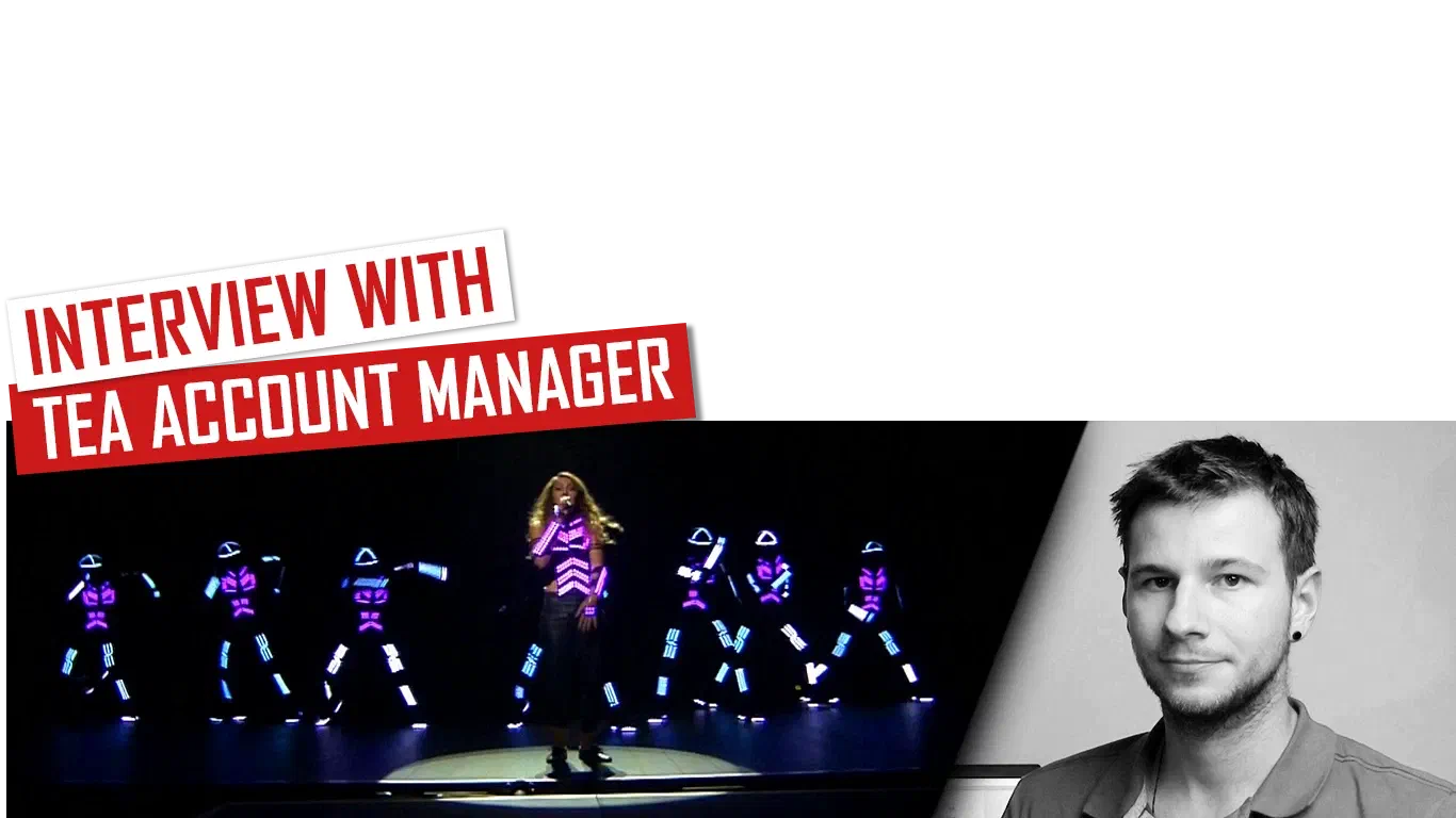 Interview with TEA Account Manager – red and white banners above Tron dancers in glowing purple and blue LED suits around a singer on a dark stage, next to a black-and-white portrait of Richie