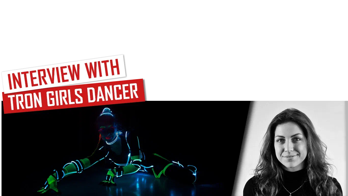 Interview with Tron Girls dancer – red and white banners above a Tron Girls dancer in a glowing LED and UV costume crouching on a dark stage, next to a black-and-white portrait of Marta