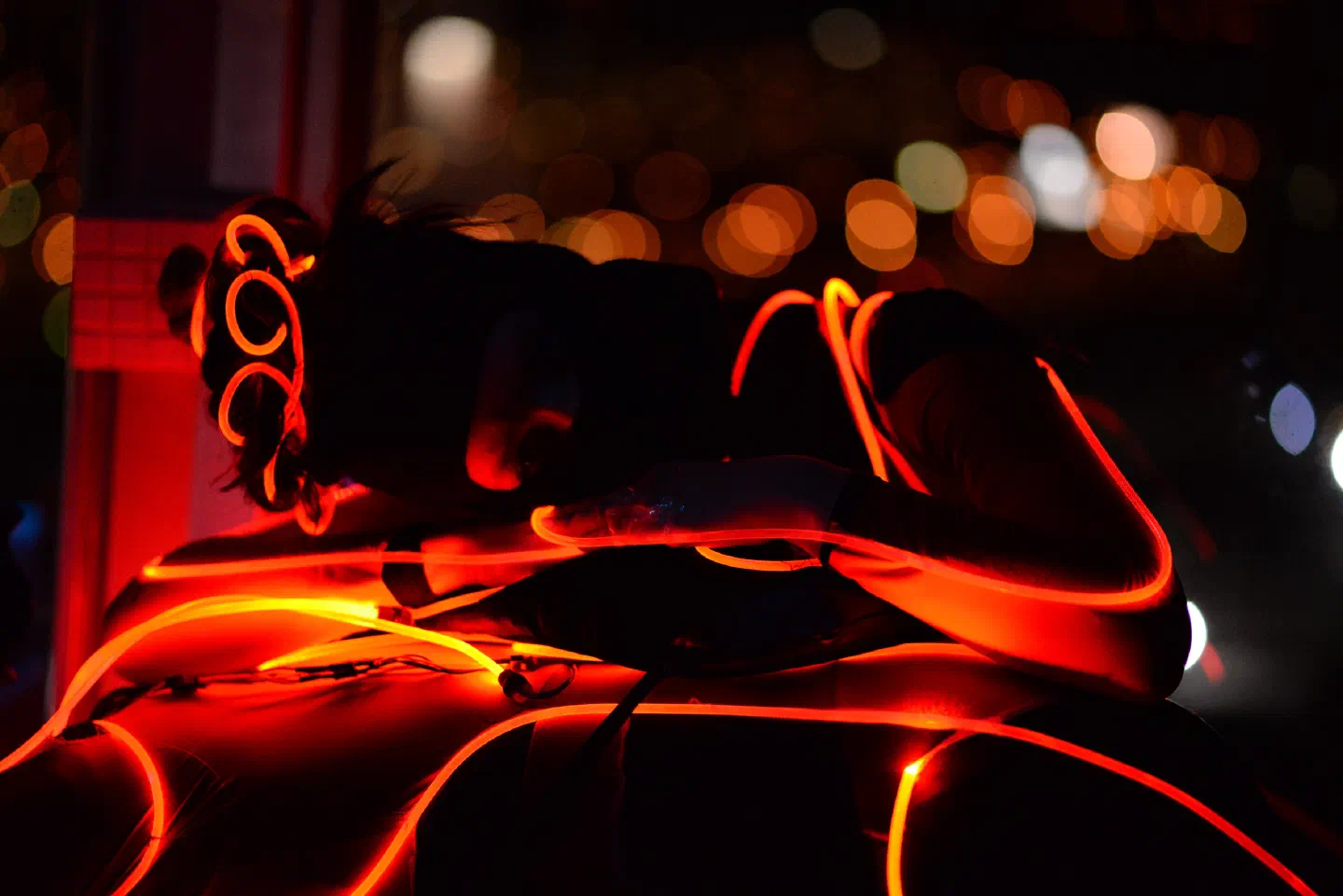 A Tron Girl in a costume lined with glowing orange-red LED strips resting after the show, with the city lights of Bratislava blurred in the background