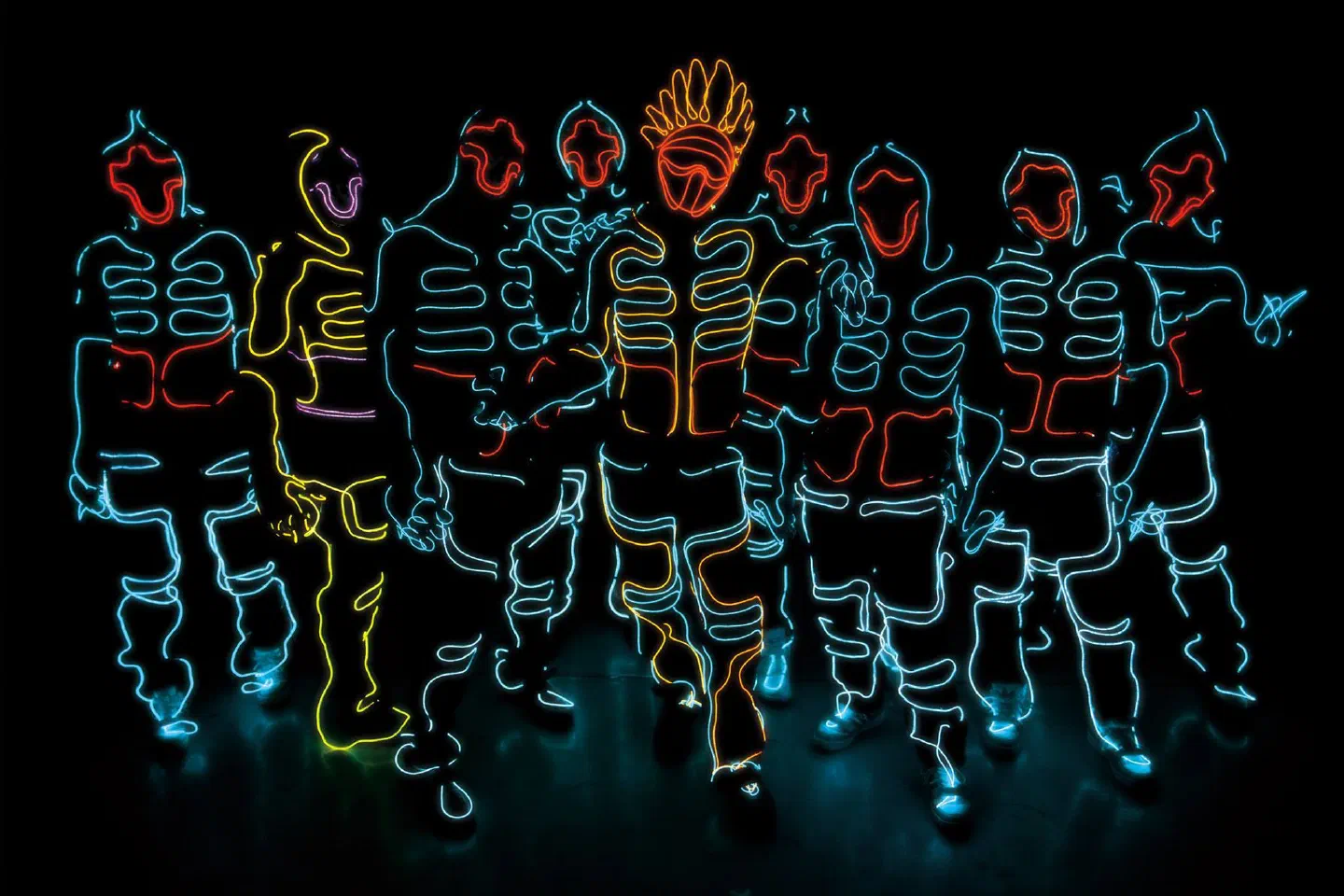 The Wrecking Orchestra crew – a row of dancers in suits outlined with glowing blue, red, yellow and orange lines standing side by side in the dark