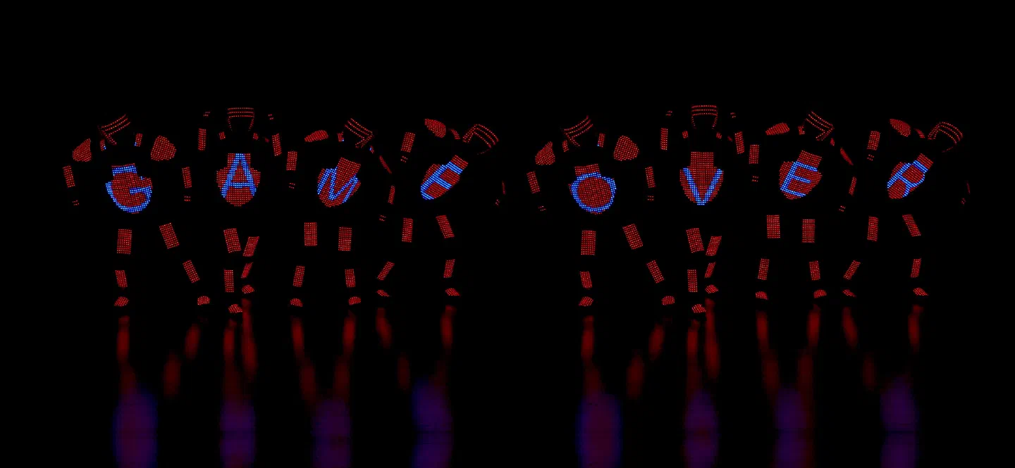 Eight dancers in red pixel LED suits, each showing one blue letter on the chest, together spelling GAME OVER