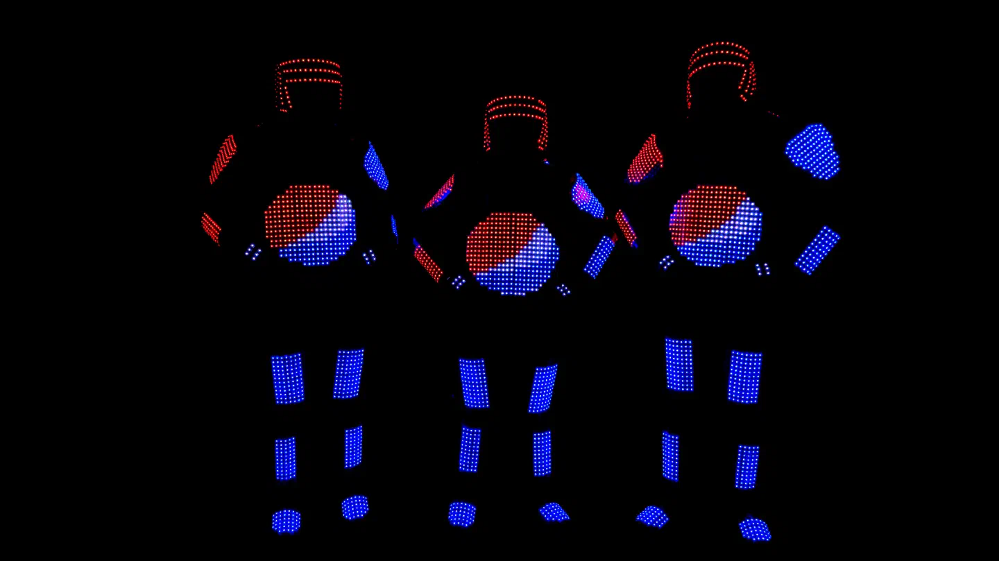 Three dancers in LED pixel suits with red pixel helmets and blue pixel arms and legs, each chest showing a round red, white and blue logo