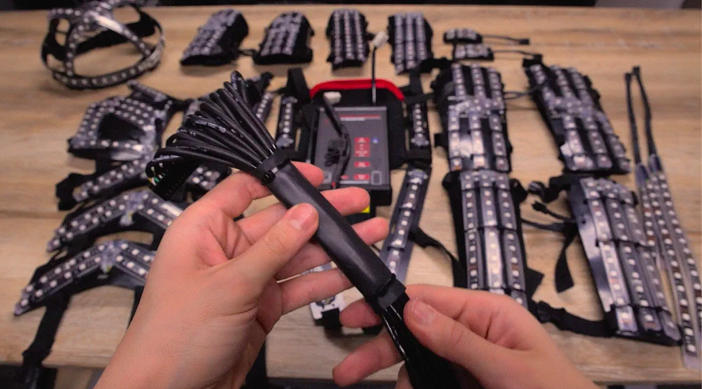 Hands holding the bundle of black cables of the Tron Dance suit, the cable ends fanning out, above the suit parts on a table