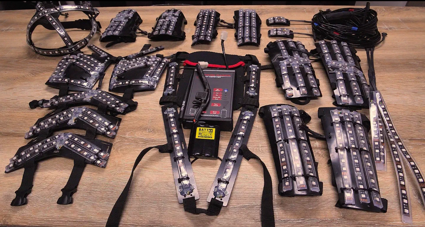All parts of the Tron Dance suit laid out on a wooden table – the body parts with LED strips, the receiver on its harness, the battery and a bundle of cables