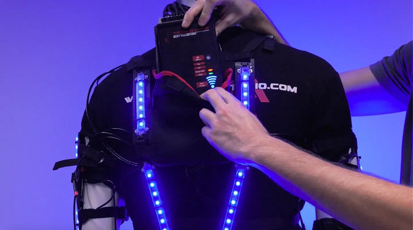 Tron Dance suit receiver in its pouch on the chest of a mannequin in an LED suit, its signal strength symbol glowing blue, with blue LED strips on the straps