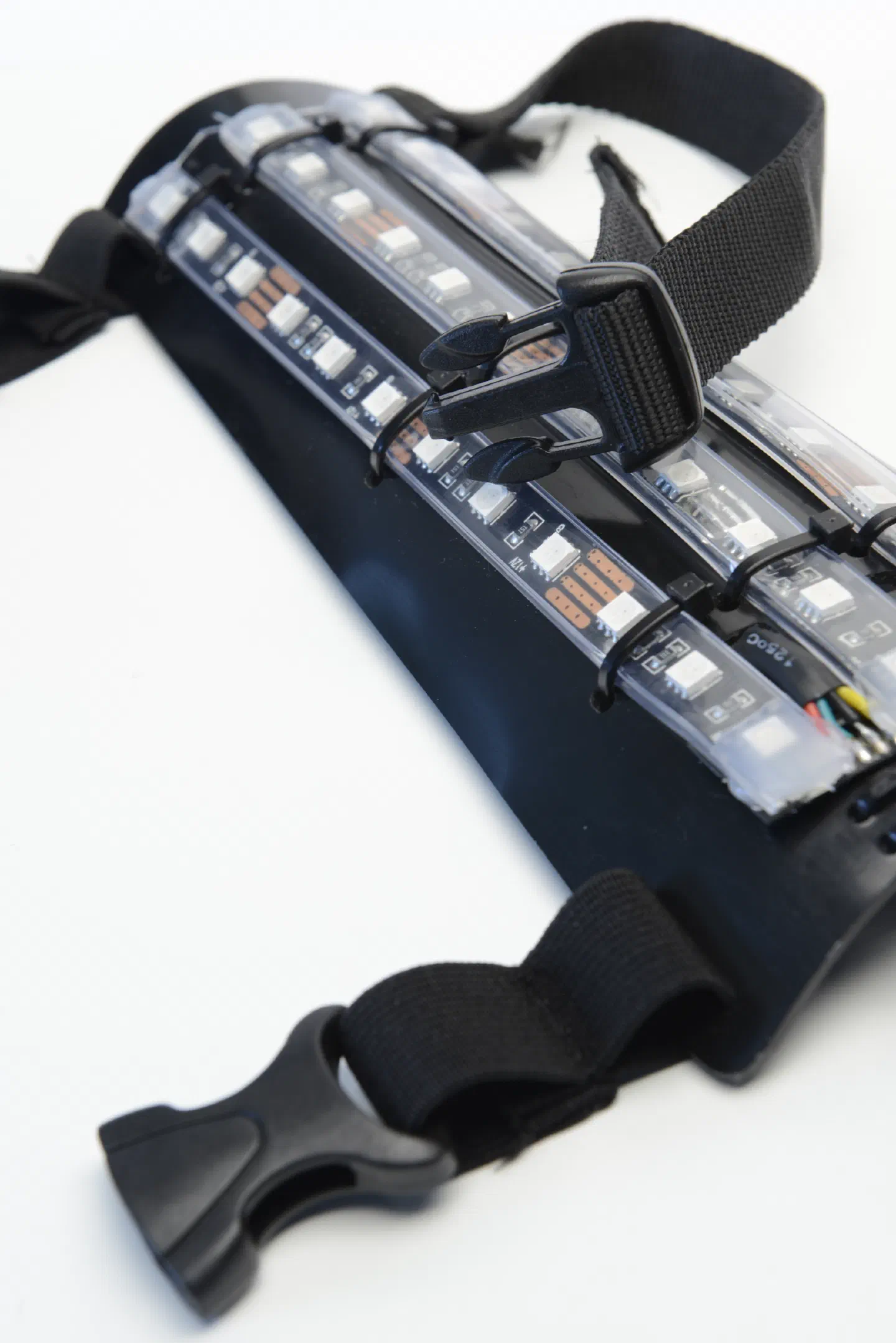 One part of the Tron Dance suit – a curved black plastic plate with three RGB LED strips held on by cable ties, and black straps with plastic buckles, on a white background