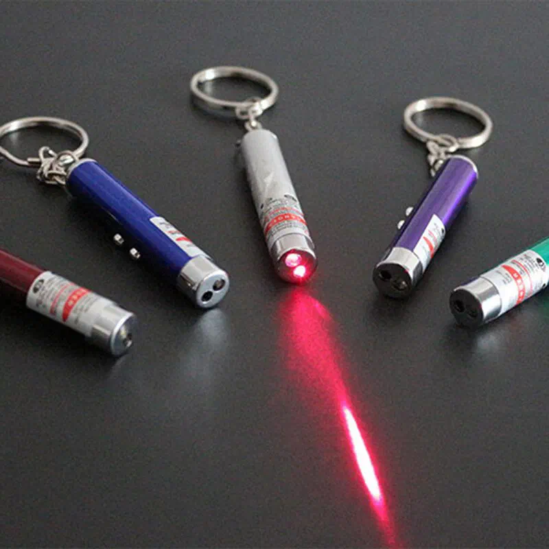 Five small laser pointer key rings in different colours on a dark table, one of them shining a red laser beam