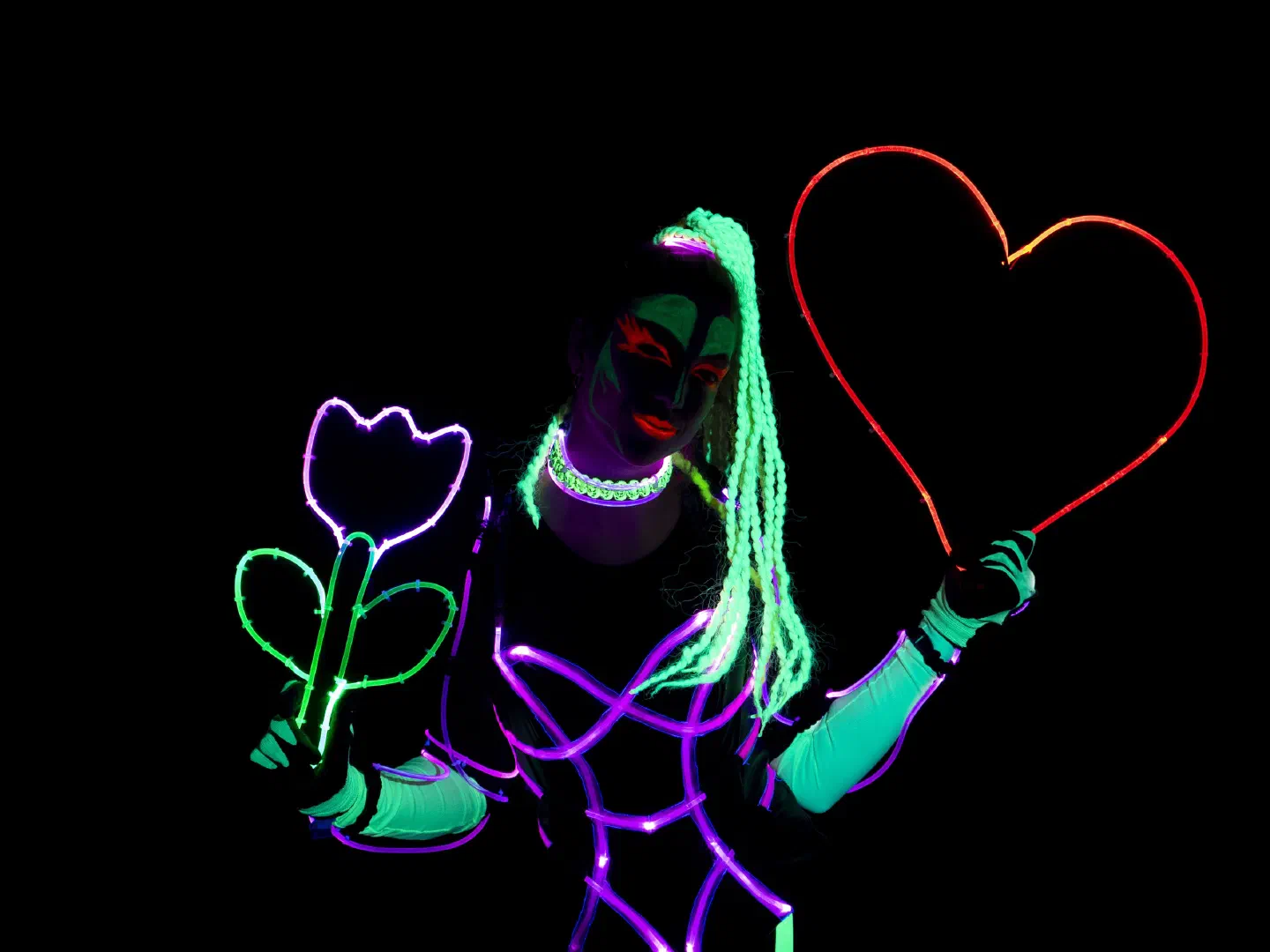 Tron Girls dancer with neon green braids, UV make-up and purple LED lines on her black costume holds a glowing flower and a red glowing heart in the dark