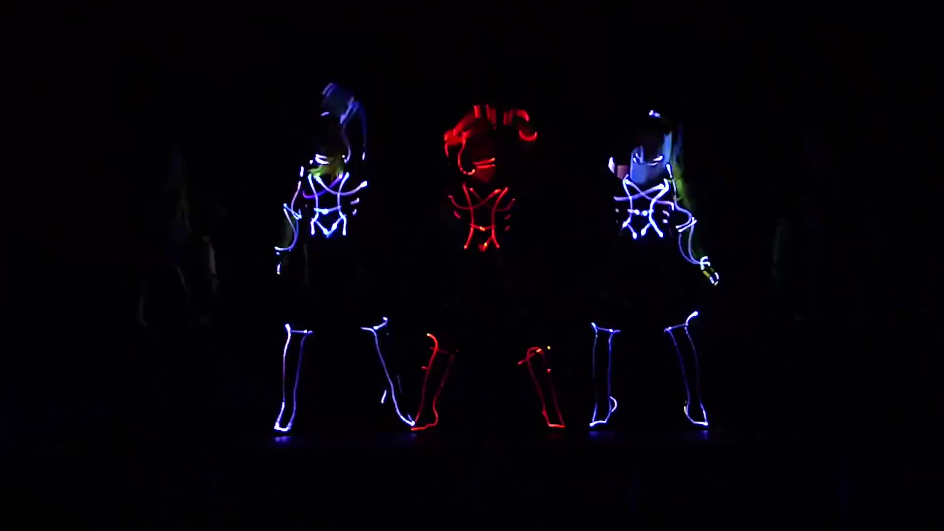 Three Tron LED dancers in glowing blue and red light suits performing on a dark stage