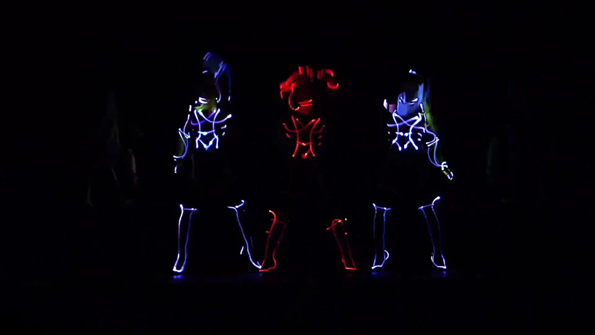 Three Tron LED dancers in glowing blue and red light suits performing on a dark stage