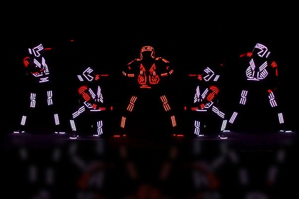Five Tron Dance Gen II dancers in white and red LED suits on a dark stage