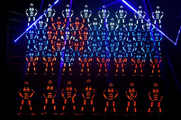 Large Tron Dance formation of LED-suited dancers in blue and orange light