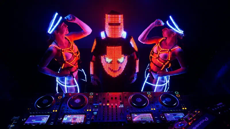 Tron DJ with an LED pixel helmet at the decks between two LED dancers