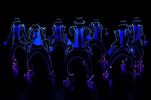 Tron Man dancers in hats and suits outlined with blue neon light