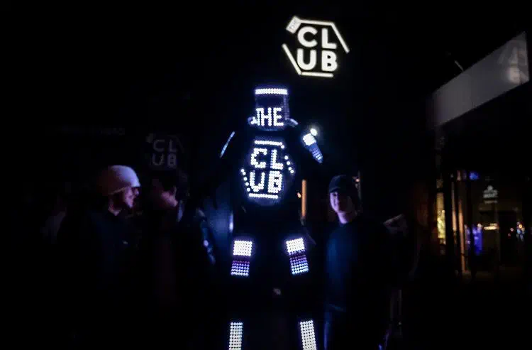 Tron Pixel Robot on stilts with a glowing LED pixel display among club guests