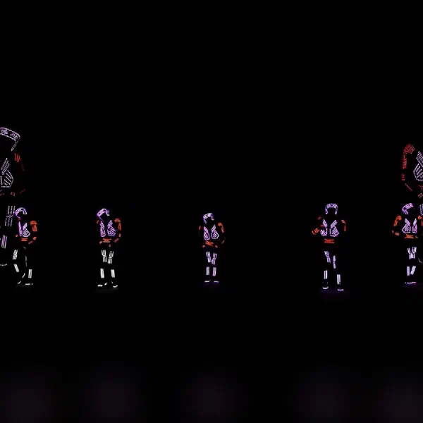 Tron Dance Gen II: seven LED dancers in violet and red light suits beside giant projected figures on a dark stage
