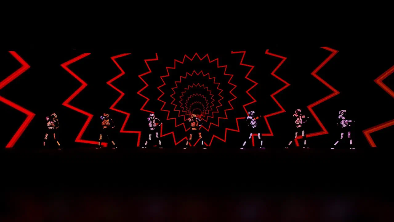 Seven Tron Dance Gen II dancers in glowing LED suits in front of a red zigzag LED-wall graphic