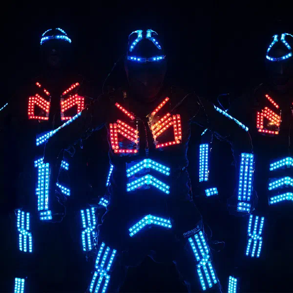 Tron Dance: close-up of three dancers in blue LED Tron suits with glowing red chest panels in the dark
