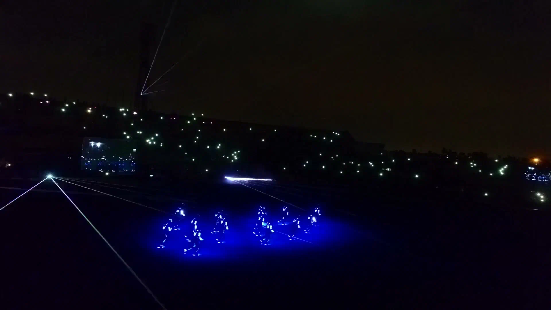 Tron Dance show: dancers in blue LED suits on a stadium field at night, with white laser beams and lights in the stands