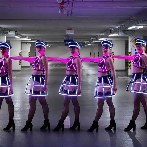 Tron Dolls: päť LED tanečníc v ružových svetelných klietkových sukniach v rade s rozpaženými rukami v podzemnej garáži