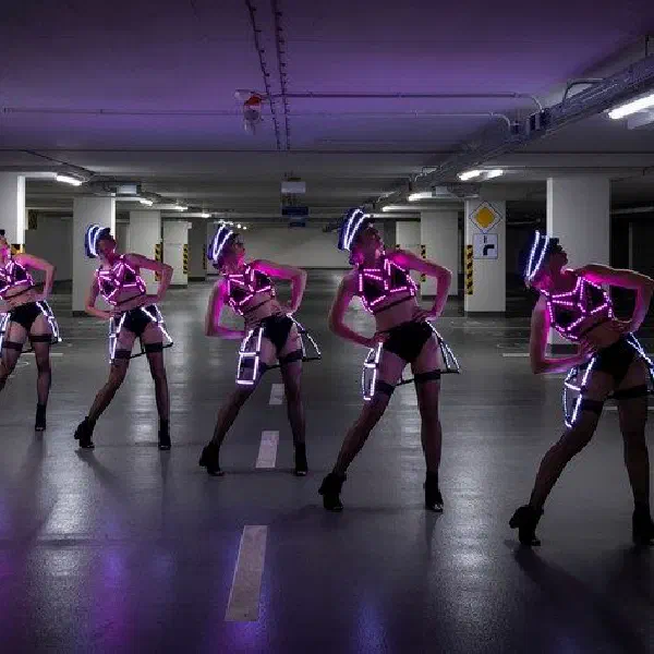 Tron Dolls: päť LED tanečníc v ružových a bielych LED kostýmoch pózuje v rade vo fialovo osvetlenej garáži