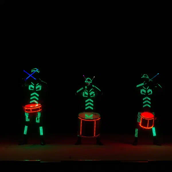 Tron Drummers: päť LED bubeníkov v zelených svietiacich kostýmoch s červenými LED bubnami, paličky prekrížené nad hlavou